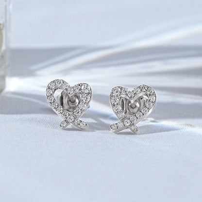 Dainty white gold heart shaped pavé diamond stud earrings displayed on a clean white surface with soft shadows.