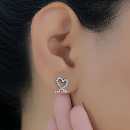 Heart shaped diamond earrings in white gold for women worn on a model ear with a close-up profile view.