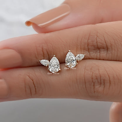 Pear cut diamond stud earrings with small accent lab diamonds held between fingers size reference nude pink nails warm skin close-up