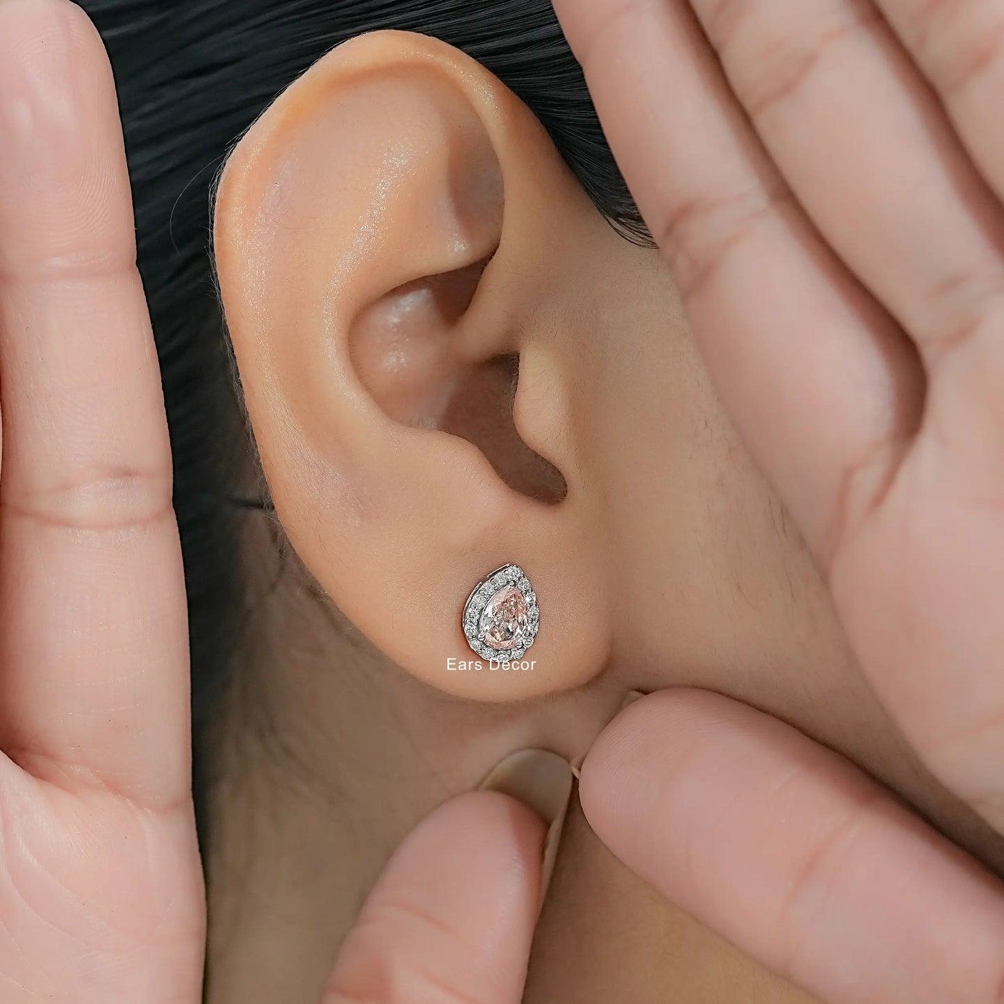 Pear cut pink gemstone diamond halo earrings small round diamond accents worn model ear close-up dark hair both hands framing face