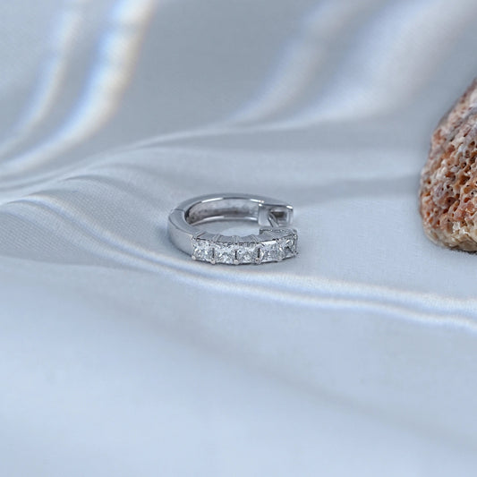 Silver ring with small stones on a textured white surface with a stone in the background