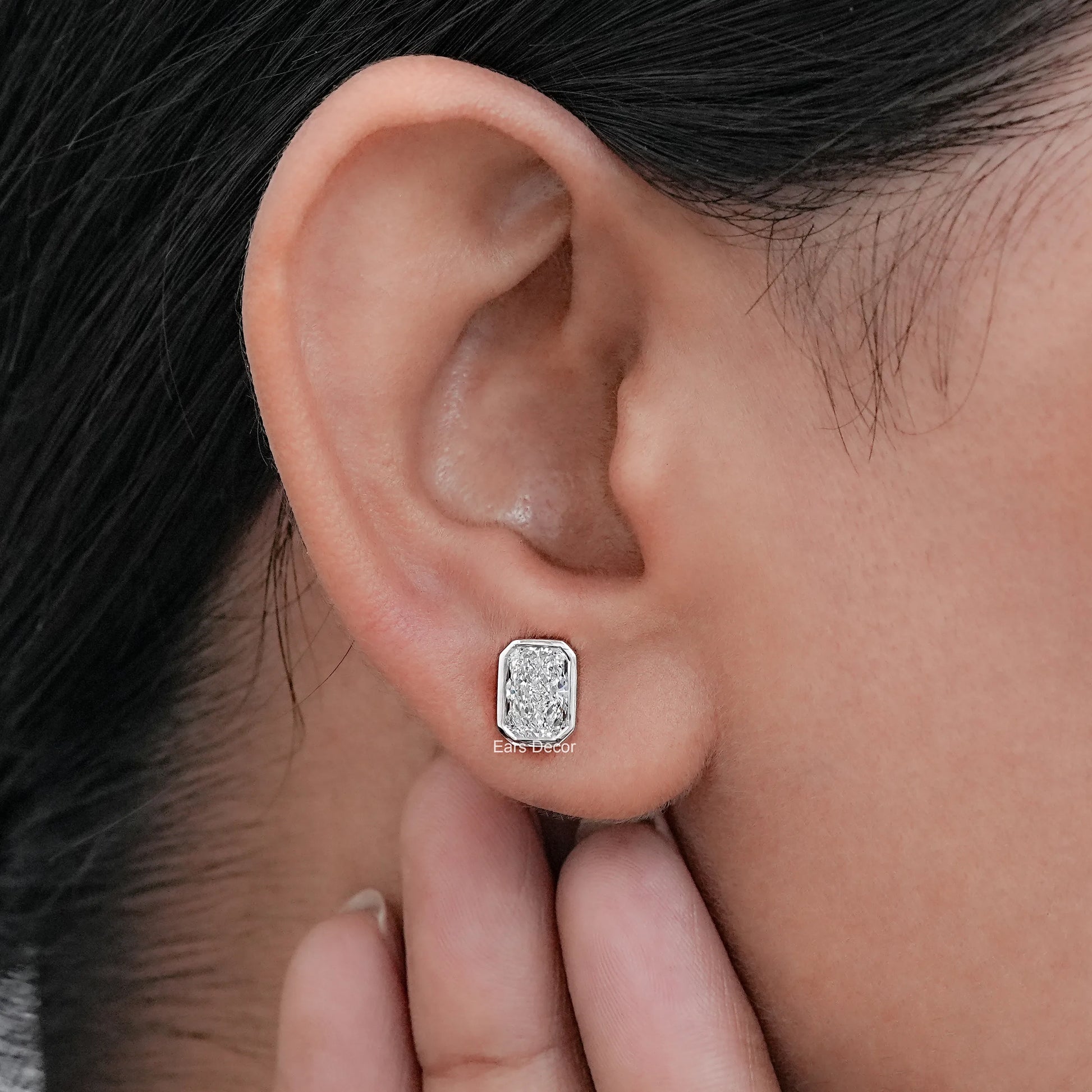 White gold radiant cut Moissanite diamond stud earring worn on model's ear close-up jewelry shot