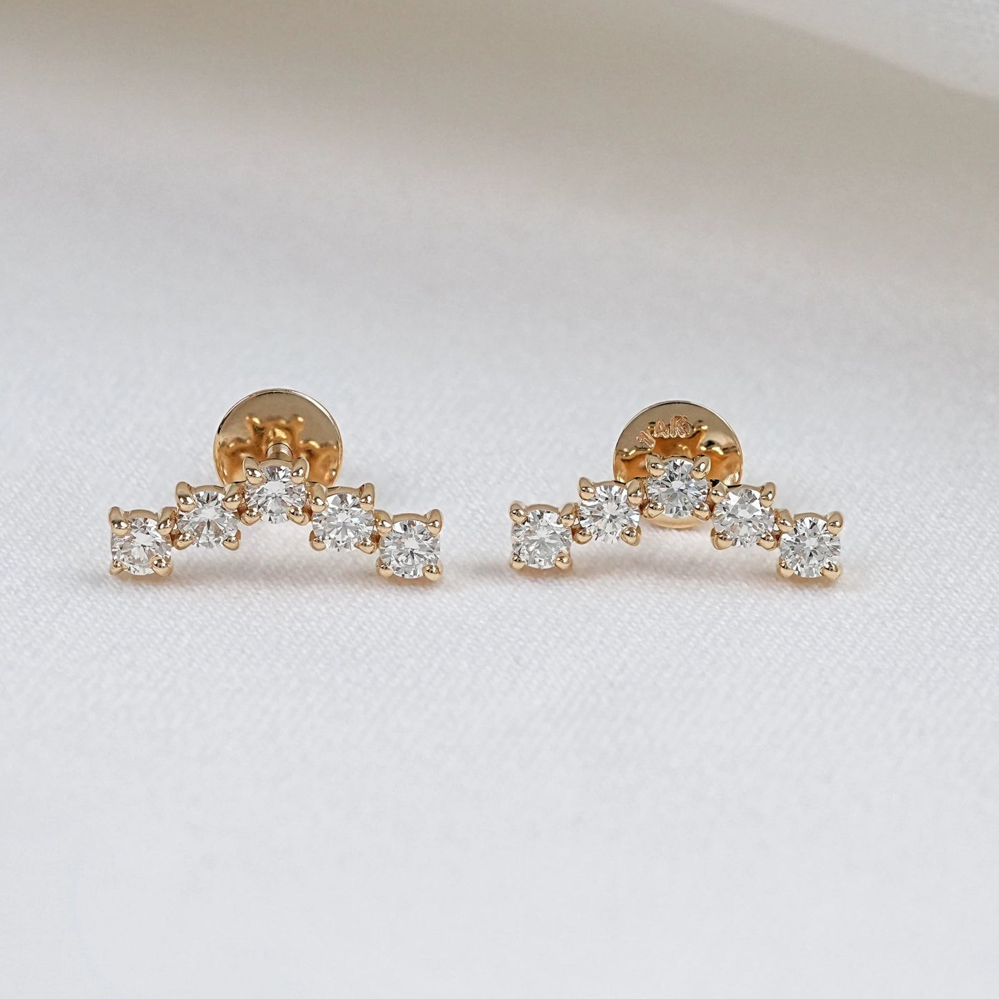 Pair of round cut five stone diamond stud earrings in yellow gold, featuring a curved arc design with prong-set lab diamonds on a white background.