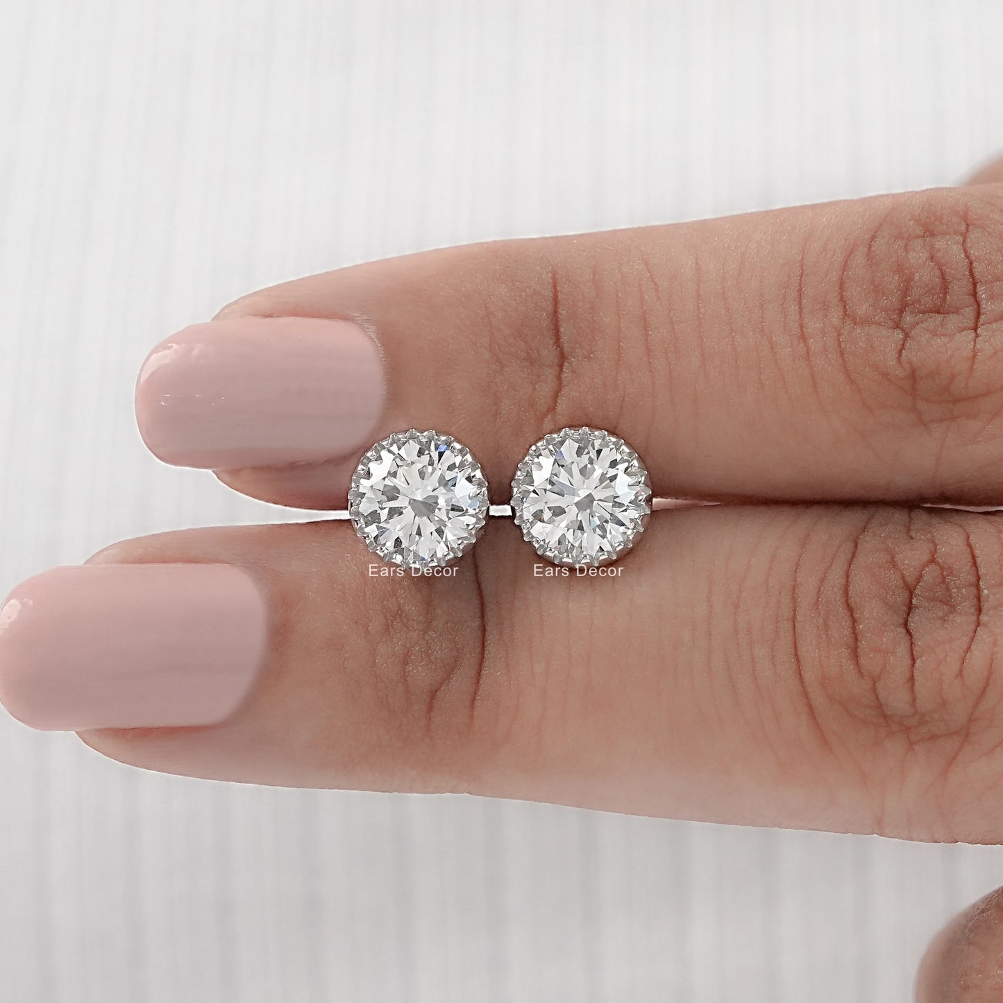 Round cut moissanite stud earrings with martini setting white gold pair displayed on model fingers nude nails close-up