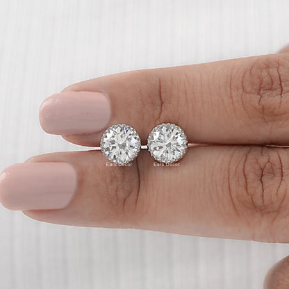 Round cut moissanite stud earrings with martini setting white gold pair displayed on model fingers nude nails close-up
