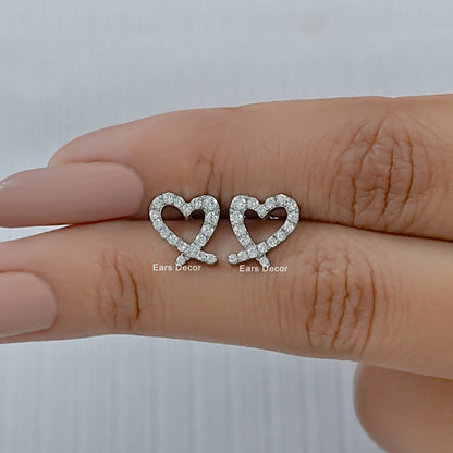Trendy minimalist heart diamond earrings for women held between fingers with a soft nude manicure.
