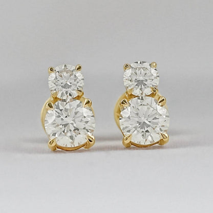 Minimalist double diamond stud earrings yellow gold second hole piercing two round brilliant stones pair flat lay grey background close-up