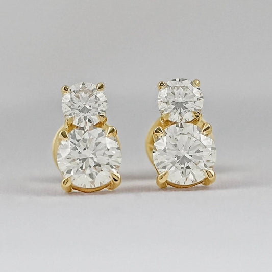 Minimalist double diamond stud earrings yellow gold second hole piercing two round brilliant stones pair flat lay grey background close-up