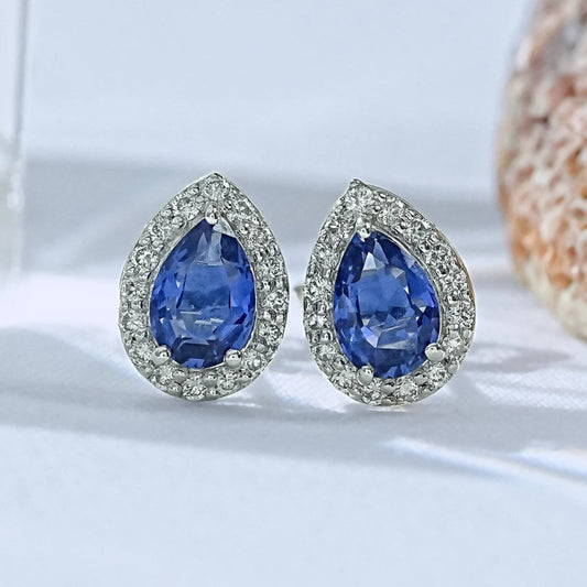 Pear shaped lab blue sapphire halo stud earrings white gold sparkling round diamond border close-up product shot light background