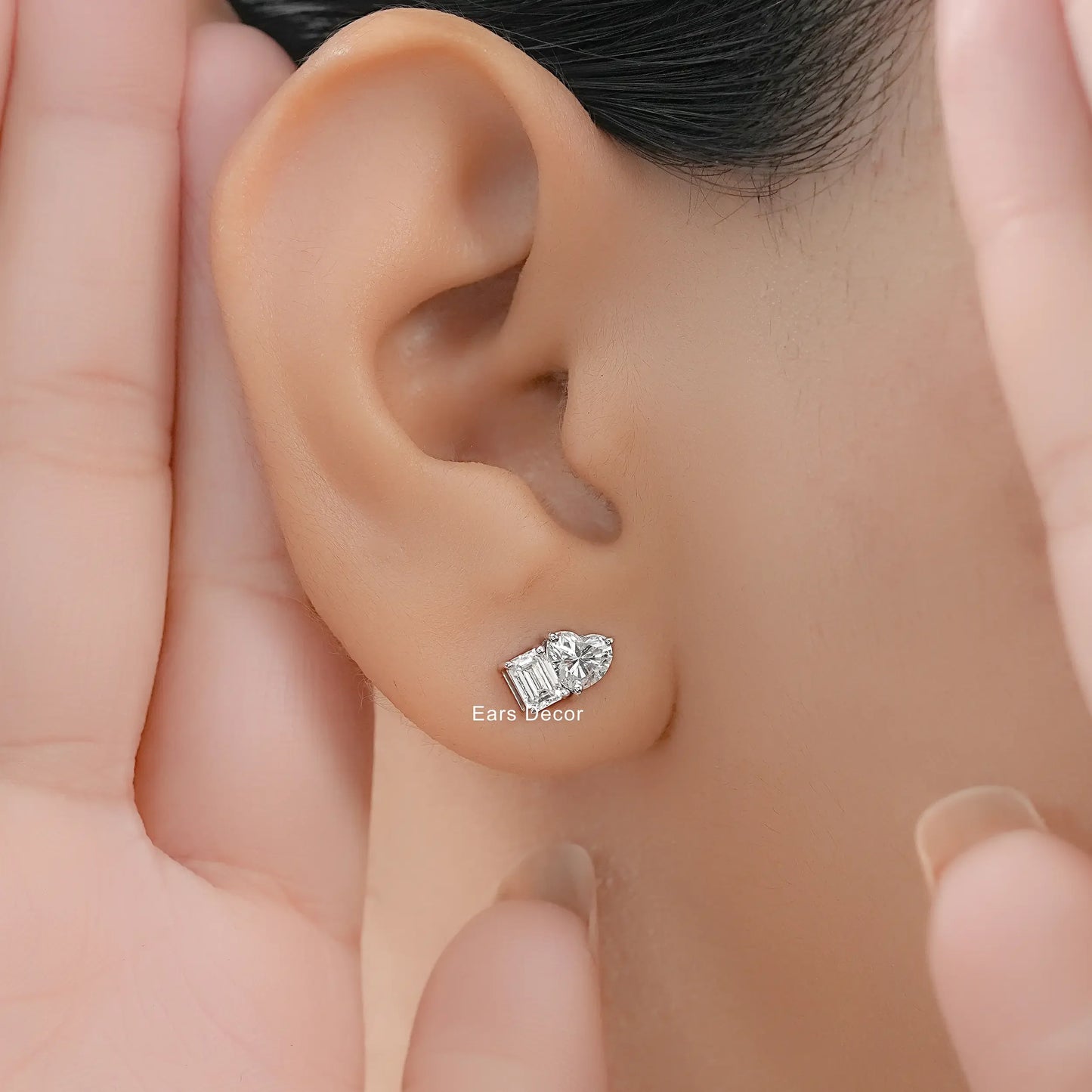 Small toi et moi heart and emerald cut diamond studs women white gold worn on model ear close-up dark hair warm skin hand cupping face