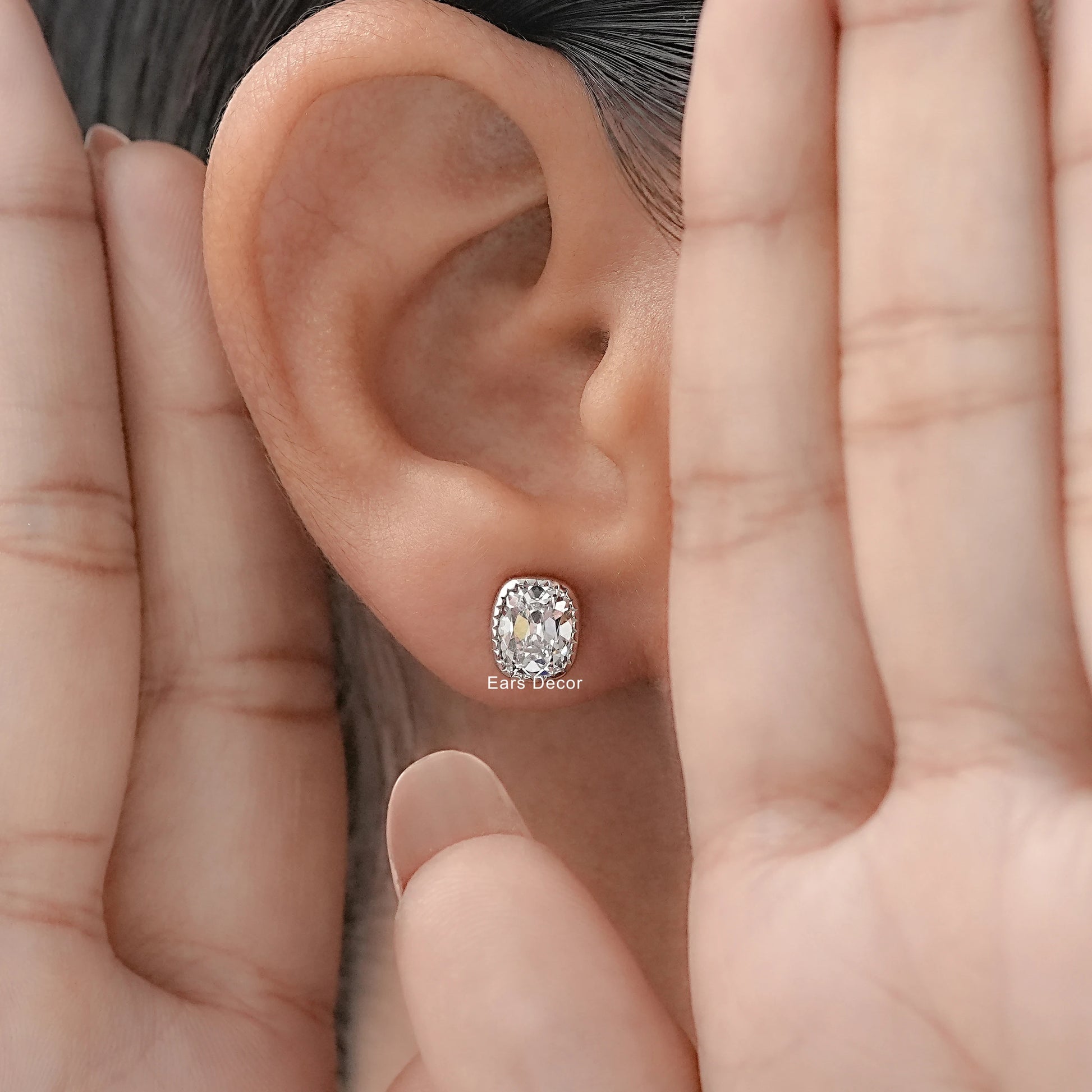 Vintage inspired cushion cut diamond stud earrings white gold milgrain bezel worn model ear both hands framing dark hair warm skin